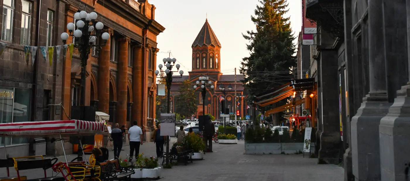 Gyumri's central street at evening: tuff facades, benches and awnings, the Holy Saviour church closing the vista