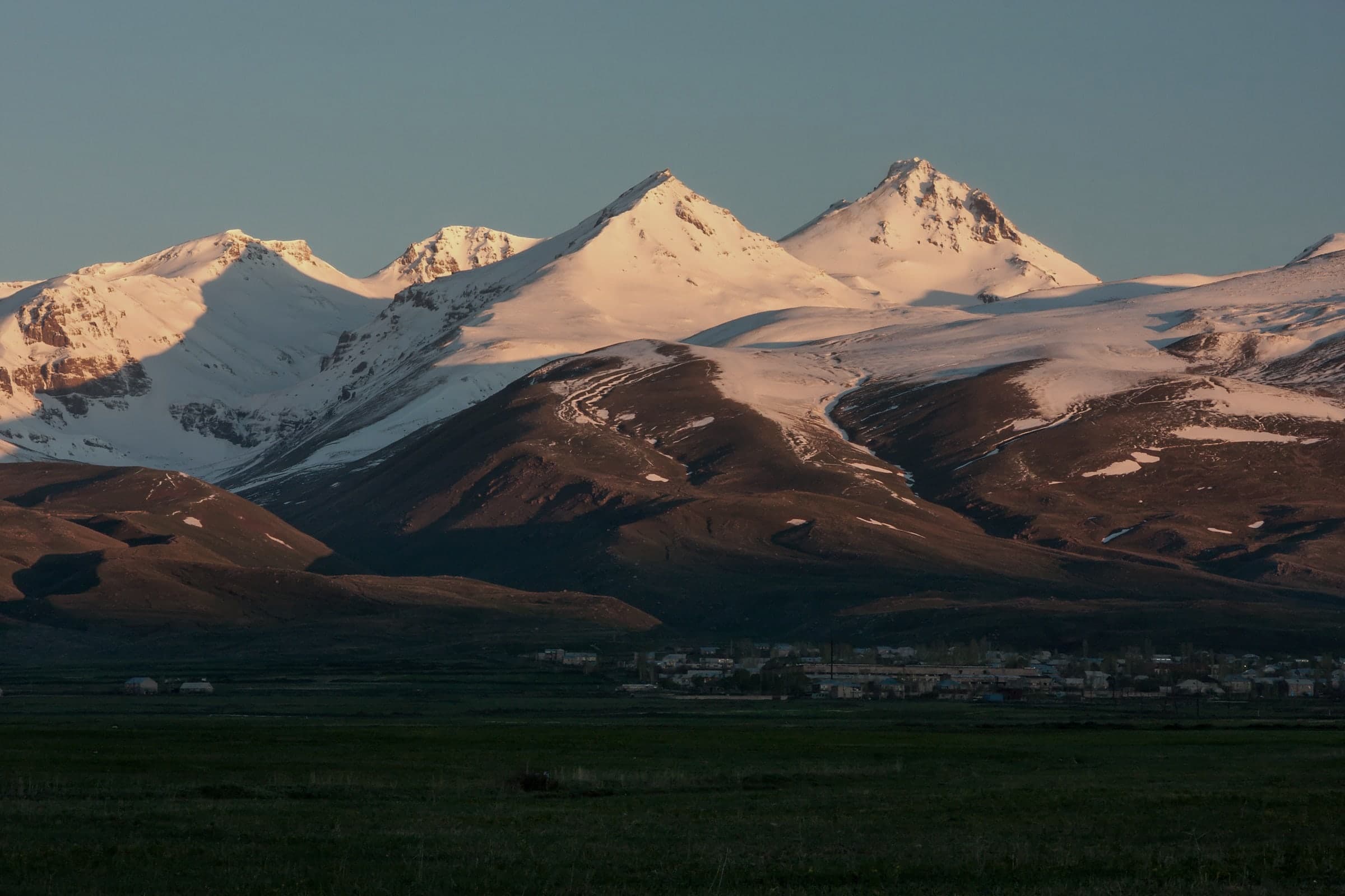 The snow-covered summits of Aragats in low light, a village at the foot of the slope