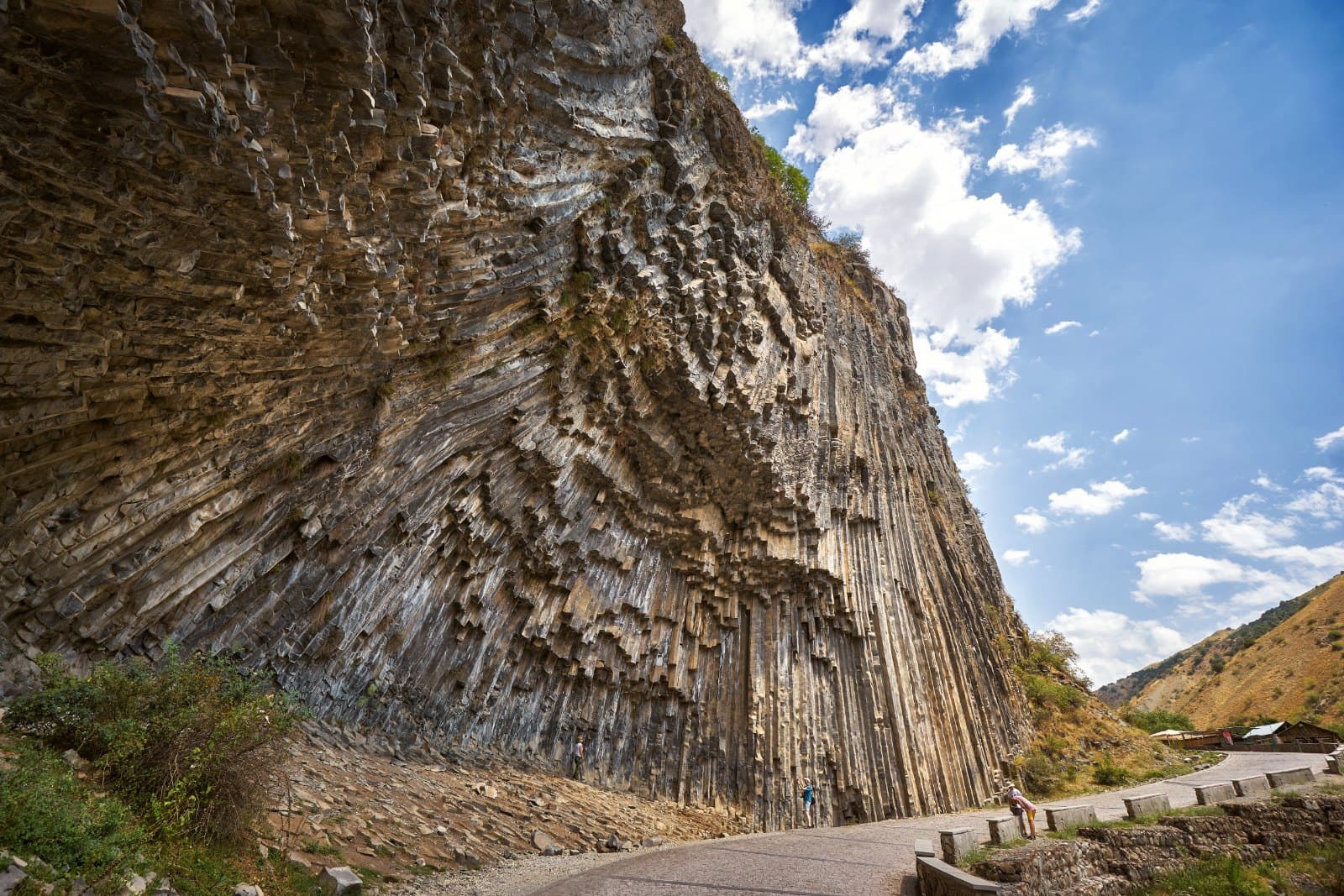 The fanned basalt columns of the Symphony of Stones curving above the gorge path, with figures small at the foot of the wall