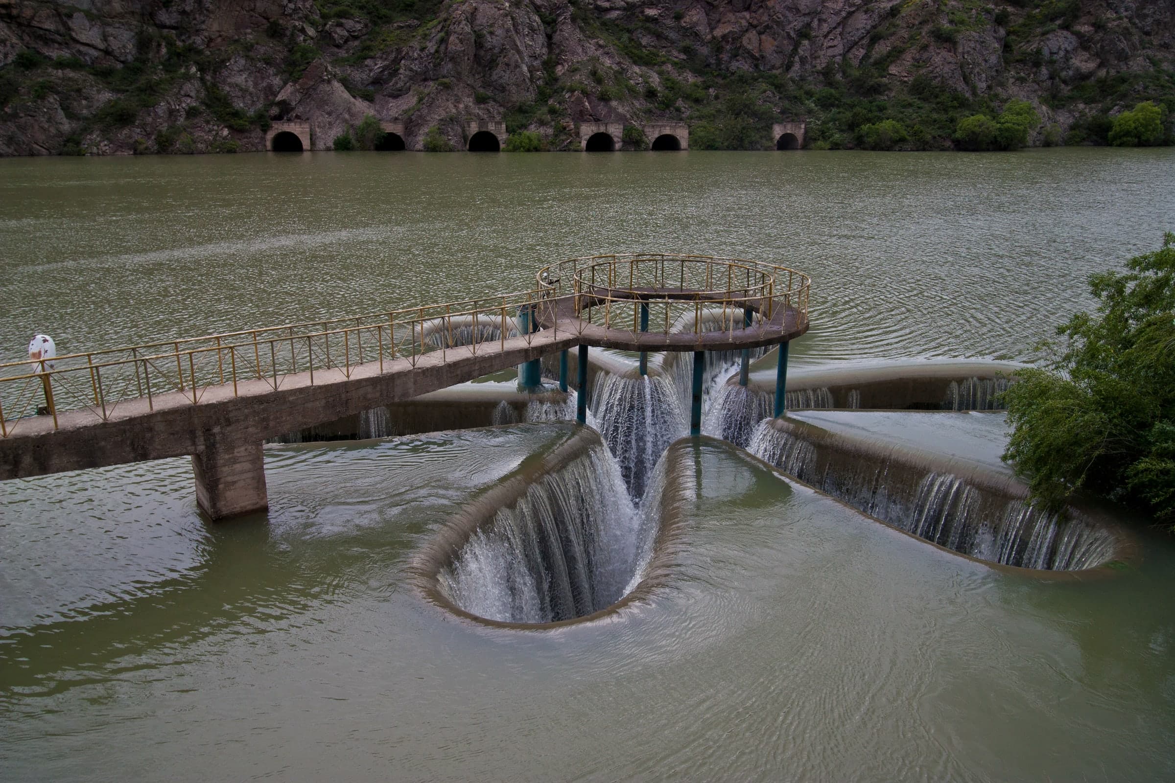 The Kechut reservoir near Jermuk, its water falling into round spillway funnels beneath a footbridge