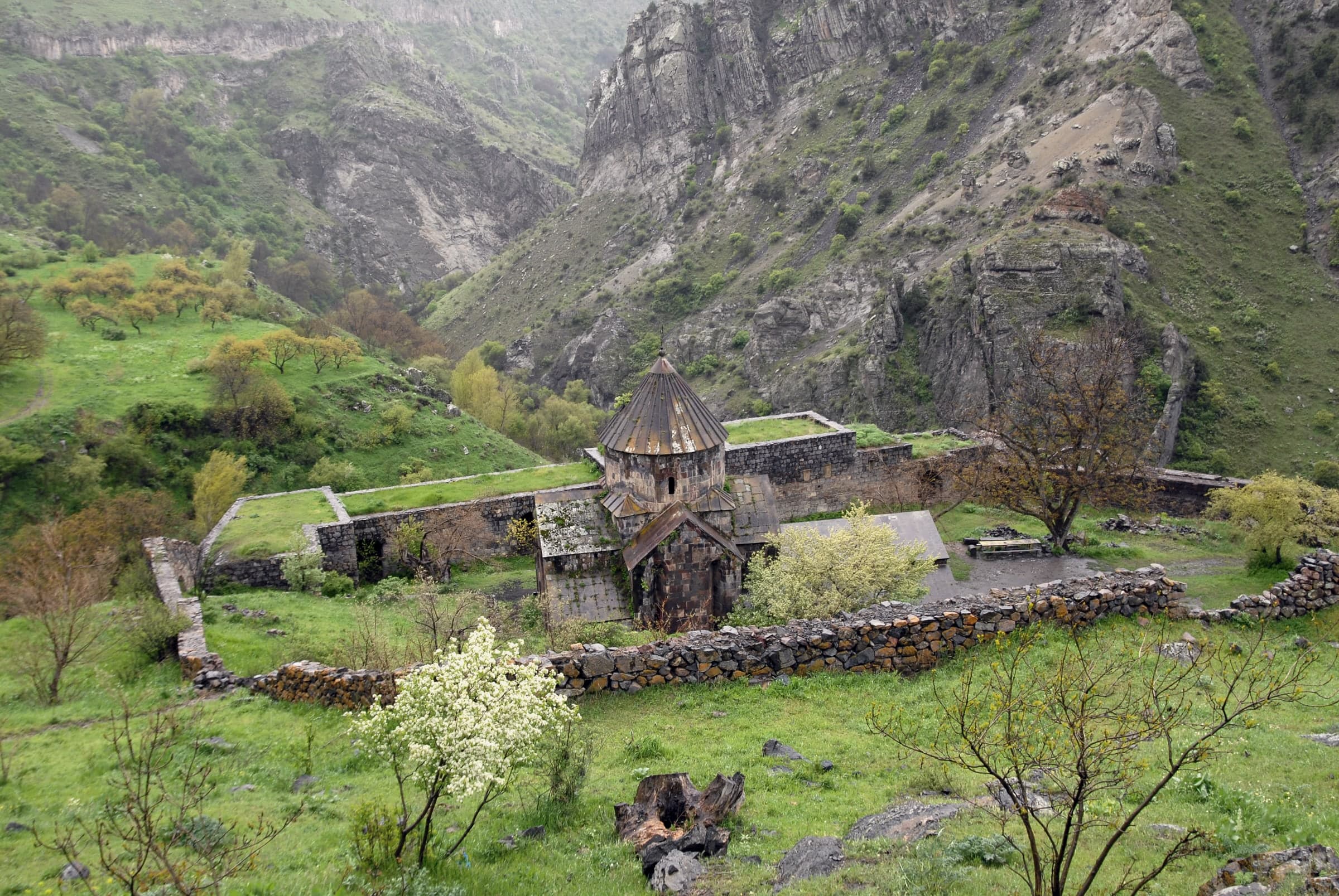 Gndevank monastery inside its stone walls, a conical-roofed church in the green gorge of the Arpa, cliffs behind
