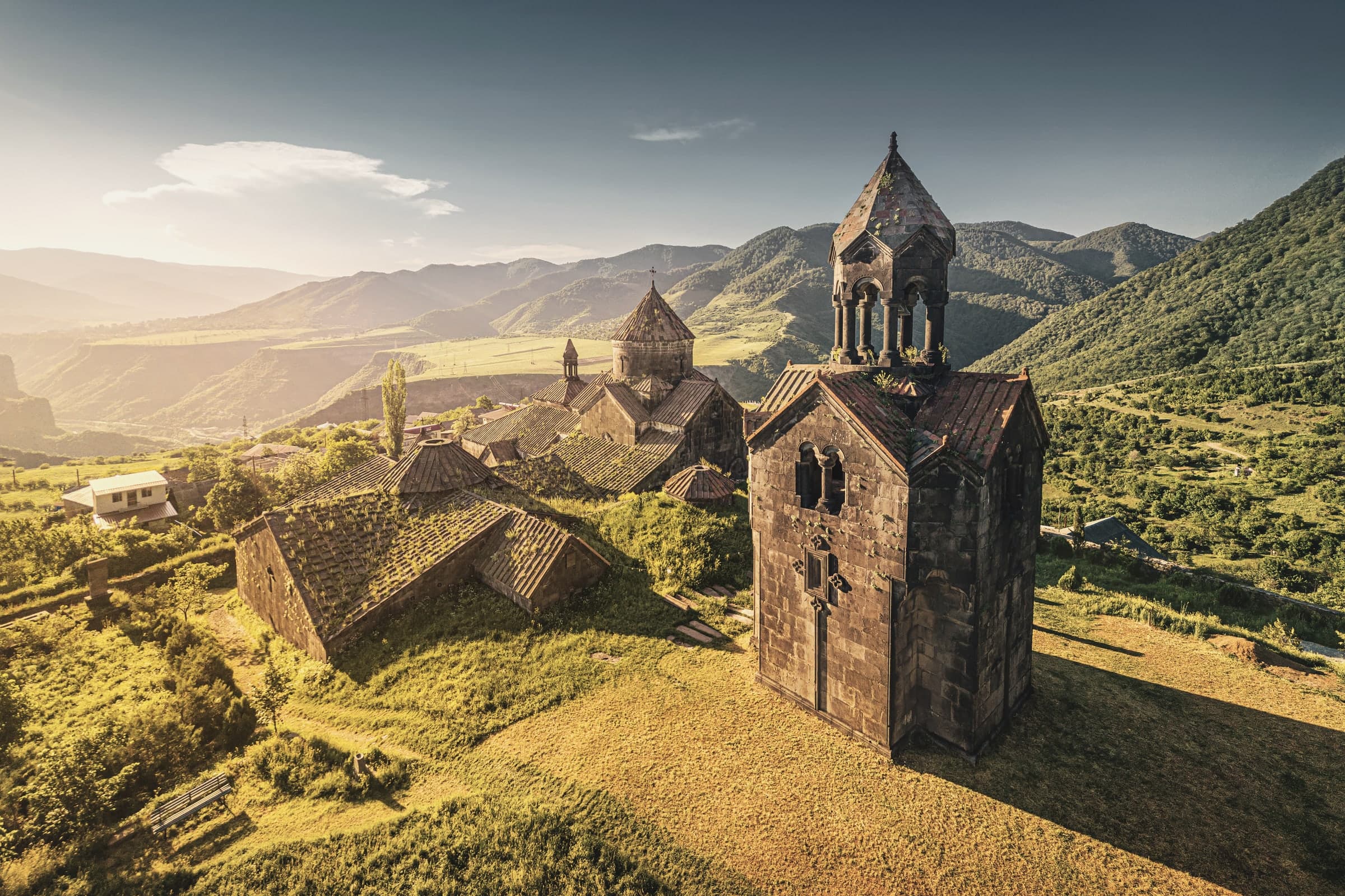 Haghpat's three-tier bell tower and church on a grassy shelf, mountains of the Debed canyon beyond, in low gold light