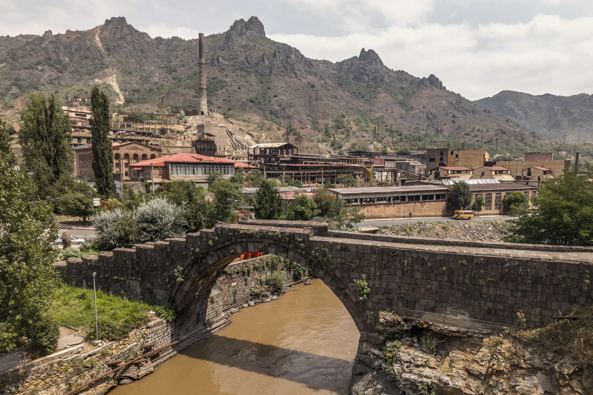 The medieval Sanahin Bridge, one stone arch over the Debed in Alaverdi, the copper works and its chimney behind