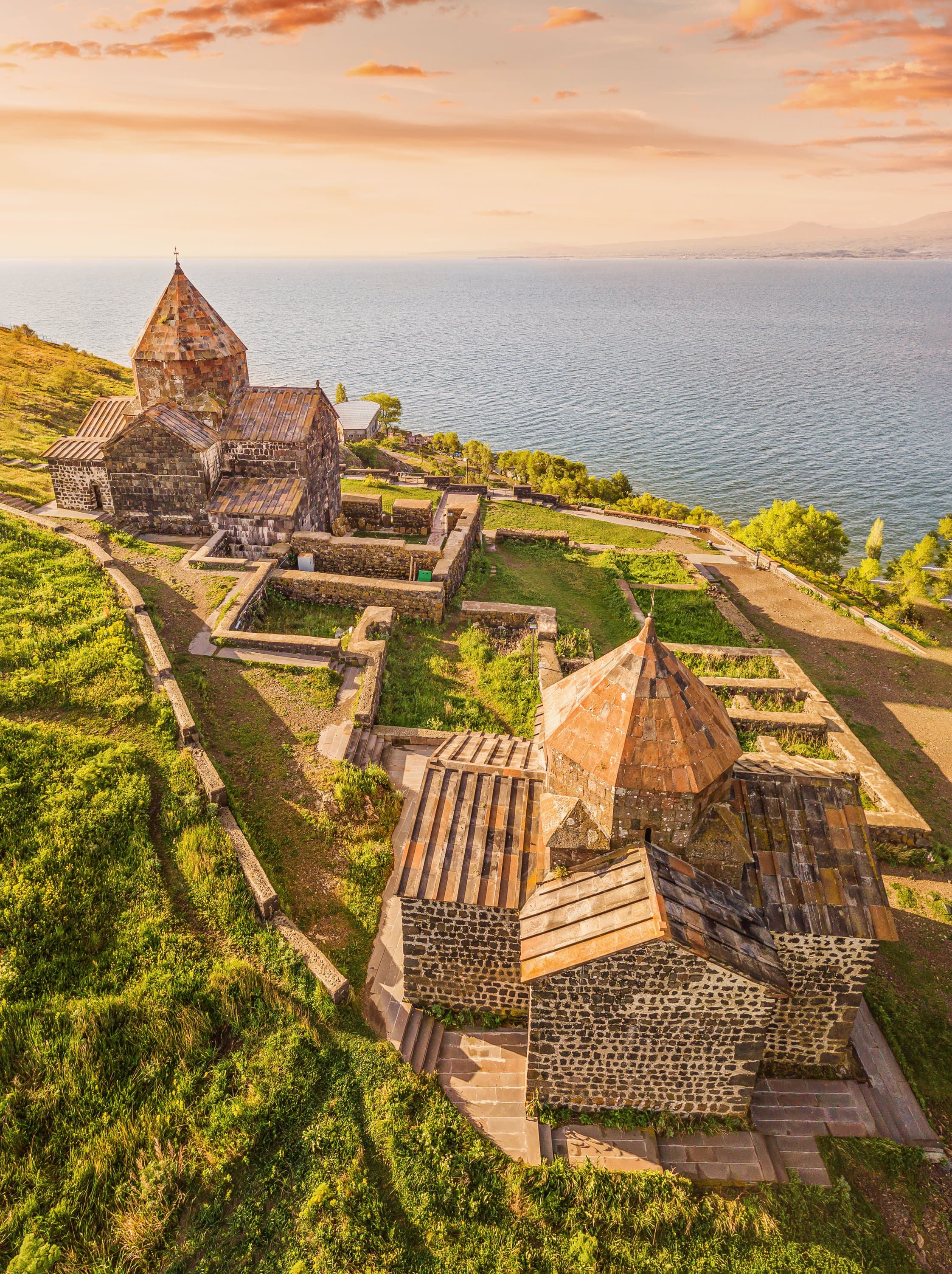 Sevanavank from the air at sunset: its two stone churches on the green headland above Lake Sevan, the water running to the far shore
