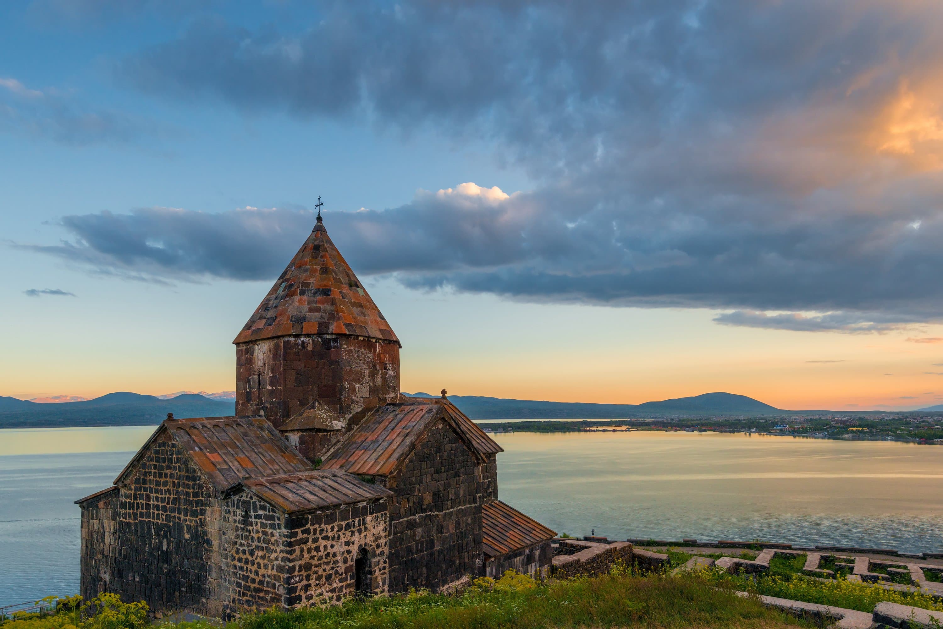Sevanavank’s dark-stone church on its headland at sunset, the lake still and pale gold behind it and low ridges on the far shore