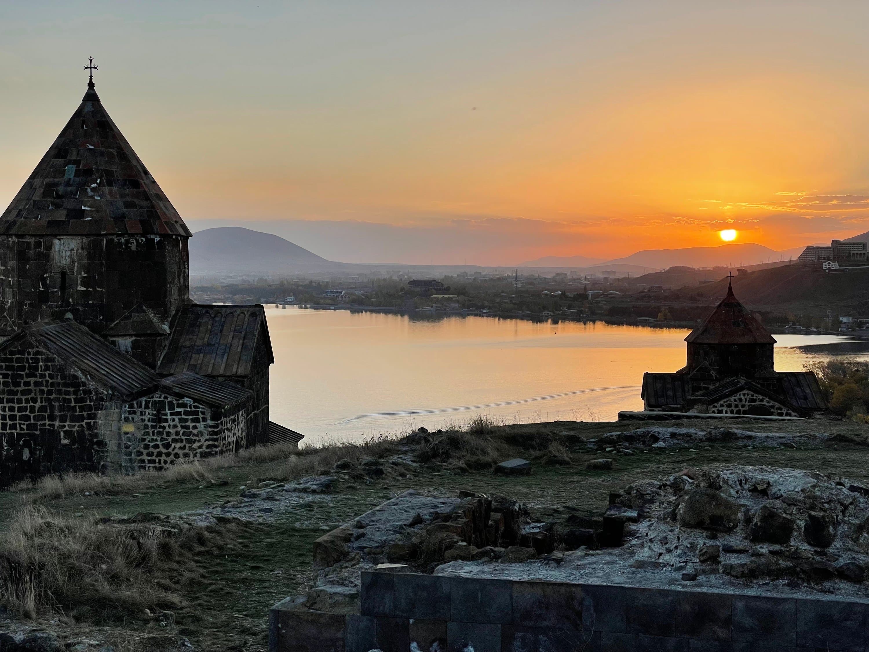 The sun setting over Lake Sevan, the water gold below Sevanavank’s smaller church, old stone foundations in the foreground