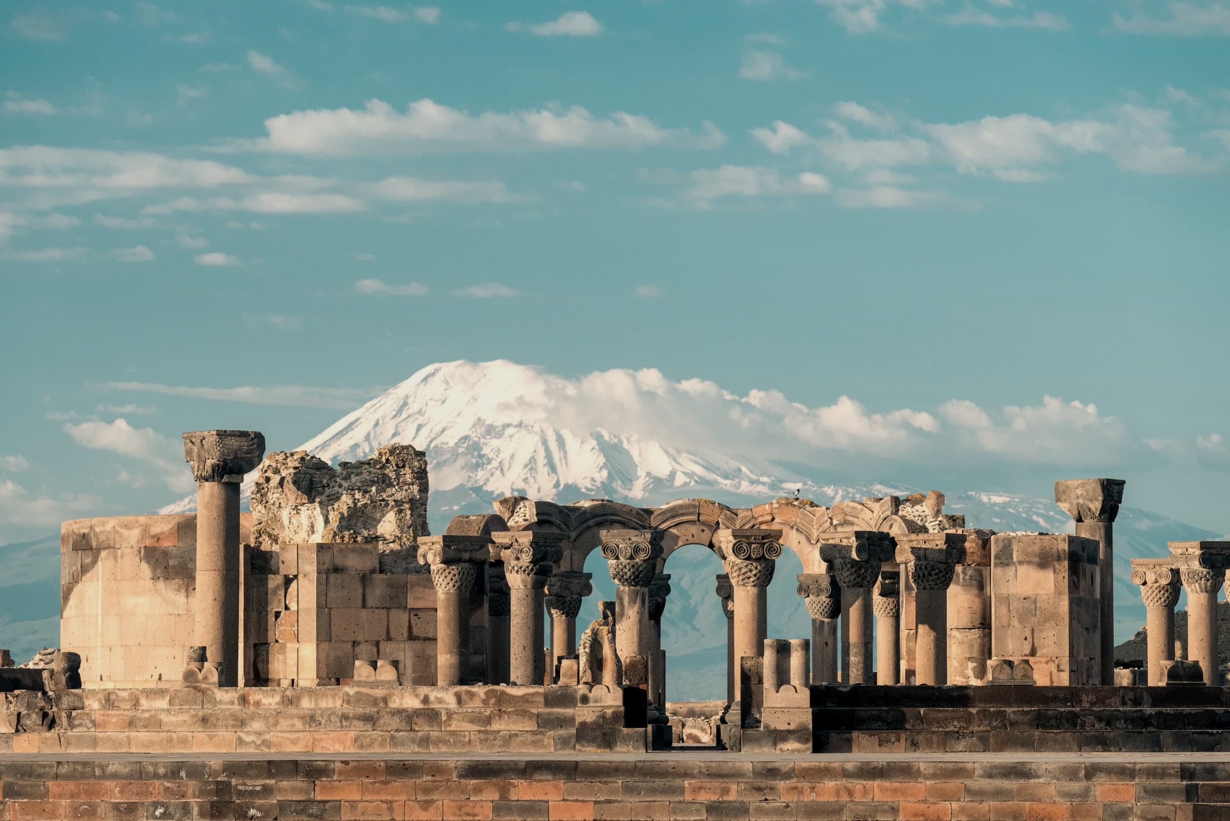 The ruined columns and arches of Zvartnots in low golden light, snow-covered Ararat rising behind them