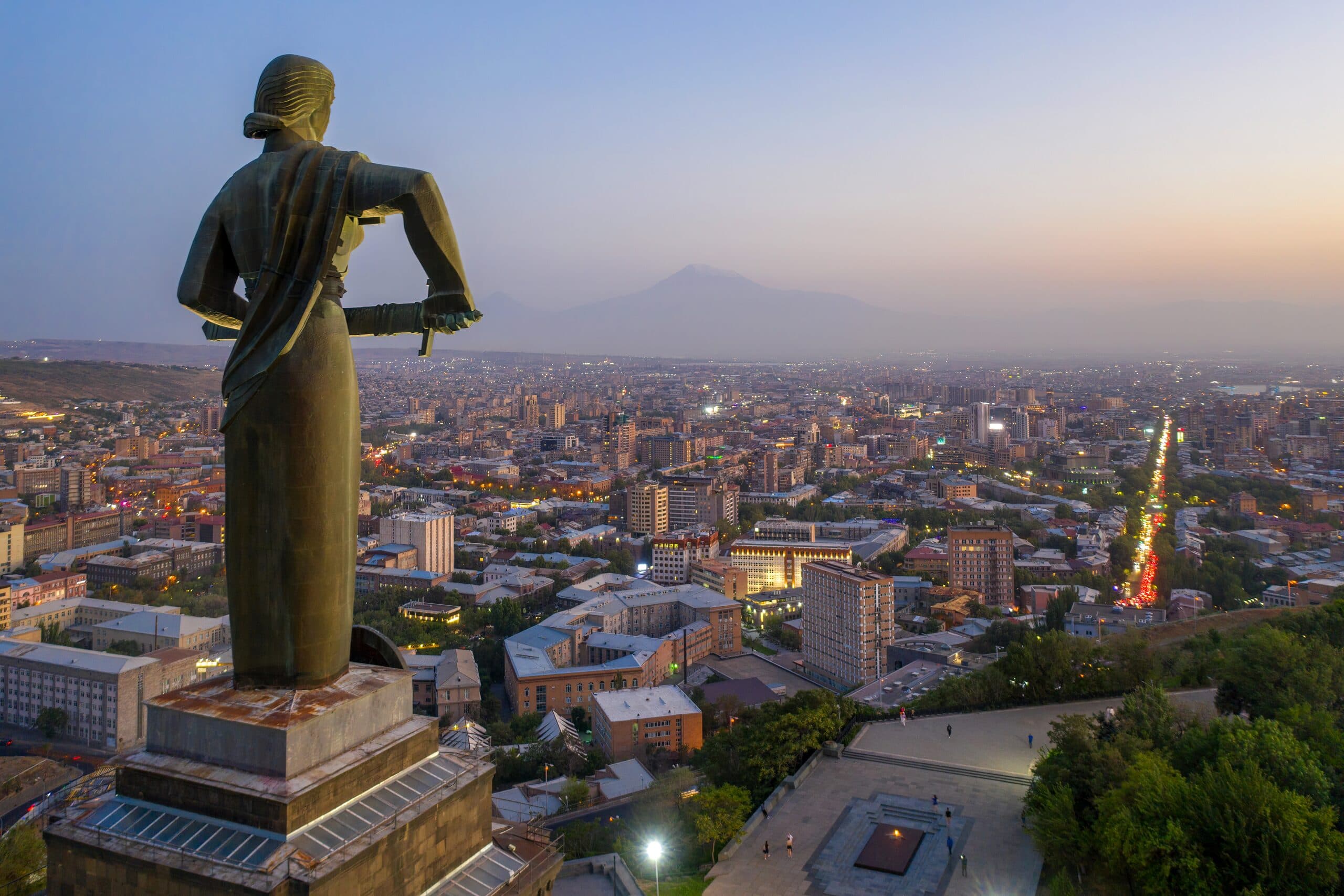 Yerevan at dusk from the Mother Armenia monument, the city lights coming on and Ararat faint behind