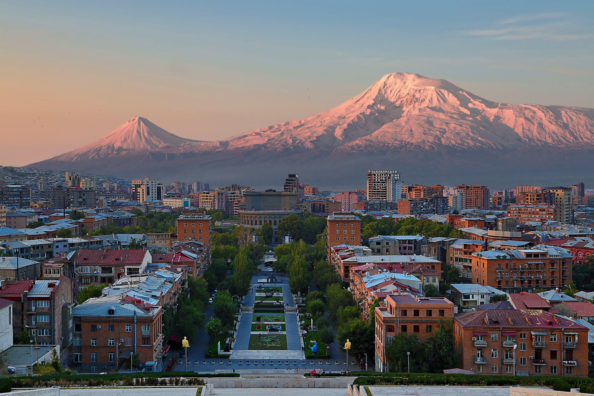 Yerevan at sunrise from the top of the Cascade: the Opera and the pink-stone streets below, both peaks of Ararat lit rose behind